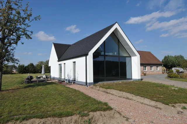 Moderne woning met witte gevel, groot glasvlak aan voorzijde en zwart dak, gelegen in groene omgeving