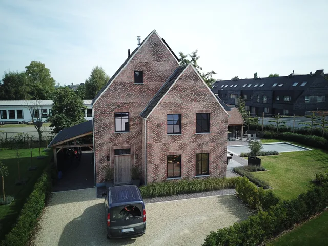 Nieuwbouw woning met rode gevelsteen, zadeldak en carport, omgeven door aangelegde tuin