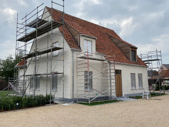 Nieuwbouw onder constructie met witte crepi gevel en oranje dakpannen, omringd door steigering