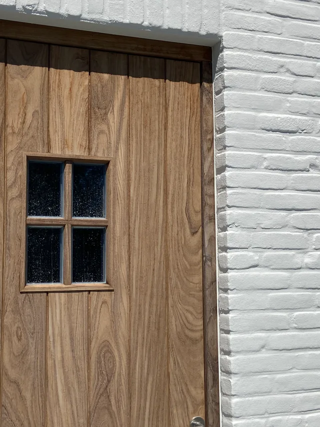 Houten deur met kruiseraam en witte stenen gevel ernaast