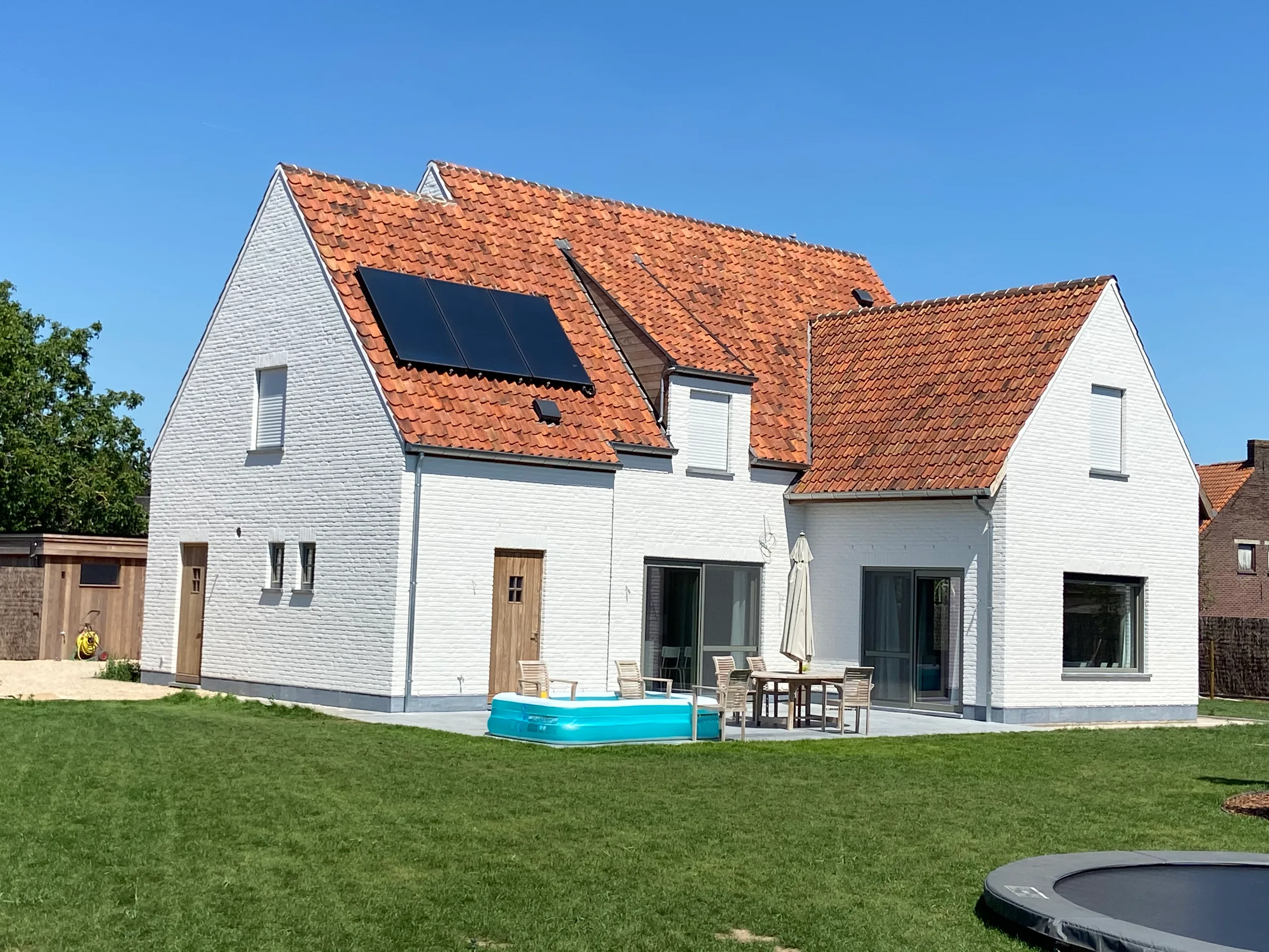 Witte nieuwbouwwoning met oranje dakpannen, zonnepanelen en dakkapel, gezien vanaf de tuin met terras