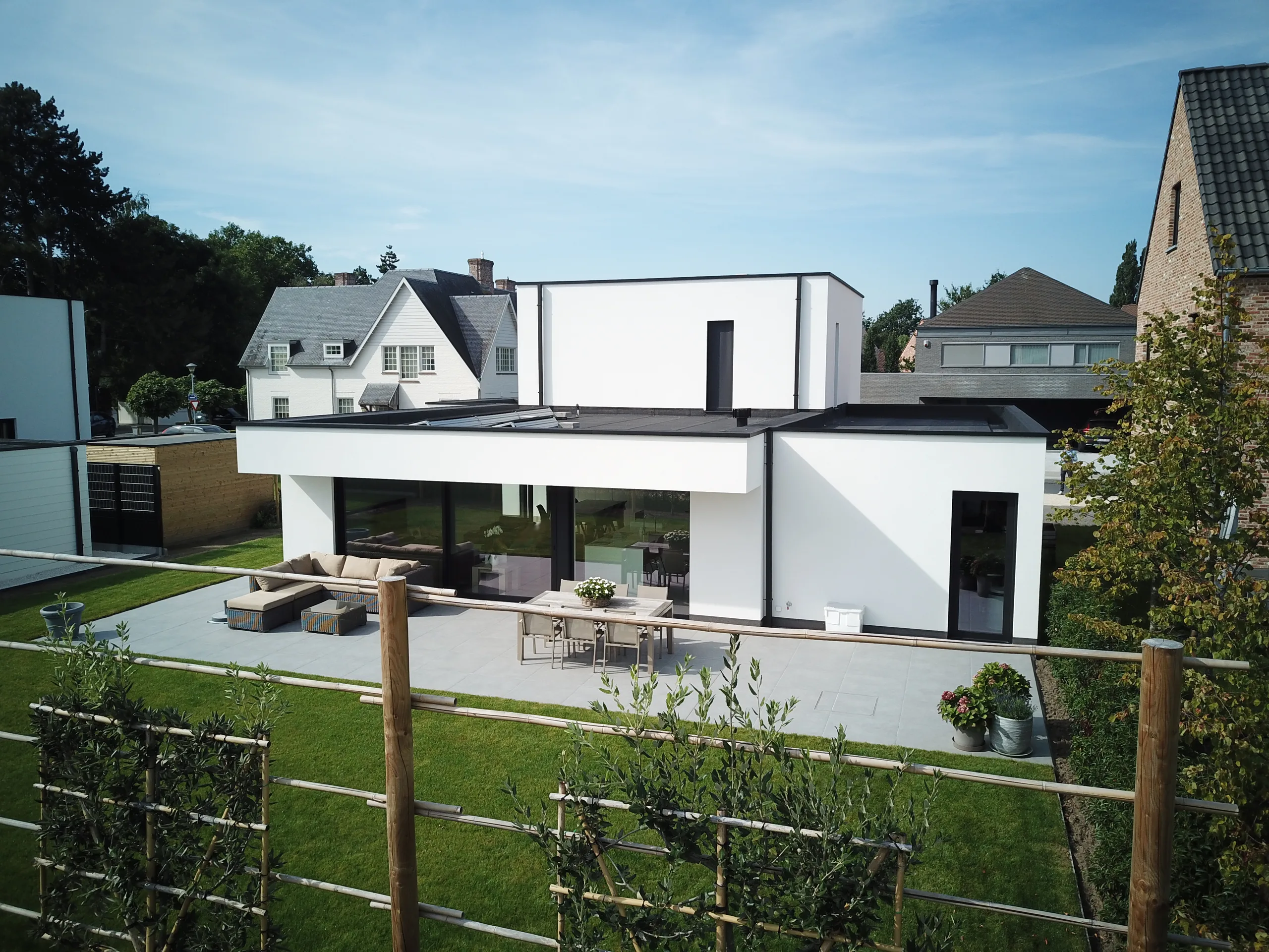 Moderne woning met witte gevel, grote glaspartijen en terras, gezien vanuit de voortuin