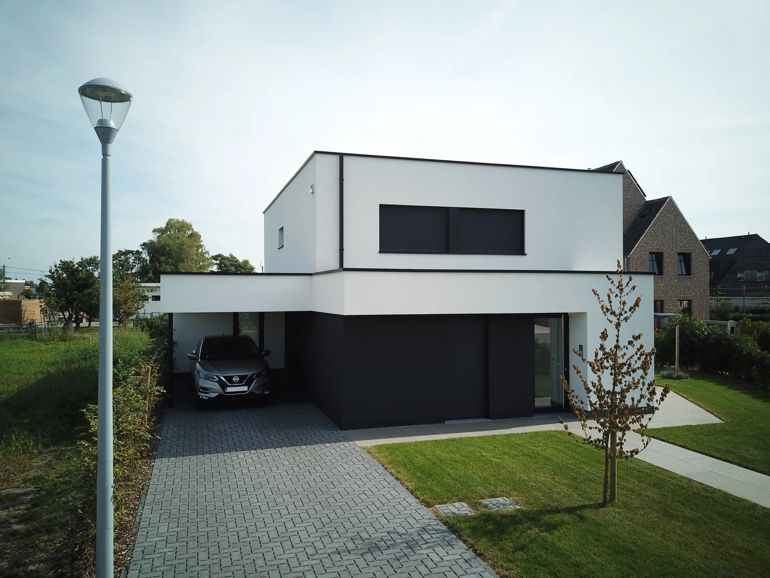Moderne woning met witte gevel, zwarte garagedeur en grote raampartijen, gezien vanaf de straat