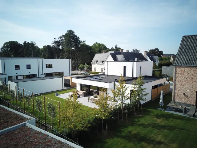 Moderne woning met witte gevel en plat dak, omgeven door aangelegde tuin met jong groen