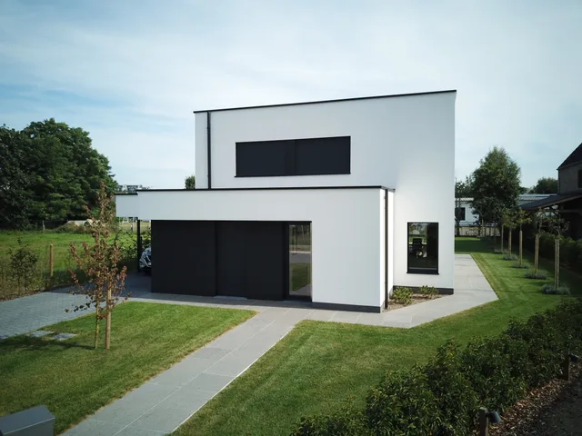 Moderne woning met witte gevel, zwarte accenten en groot glaspartijen in groene omgeving