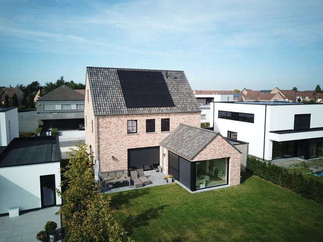 Nieuwbouwwoning aan de tuinzijde met rode gevelsteen, grote raampartijen en zonnepanelen op het dak