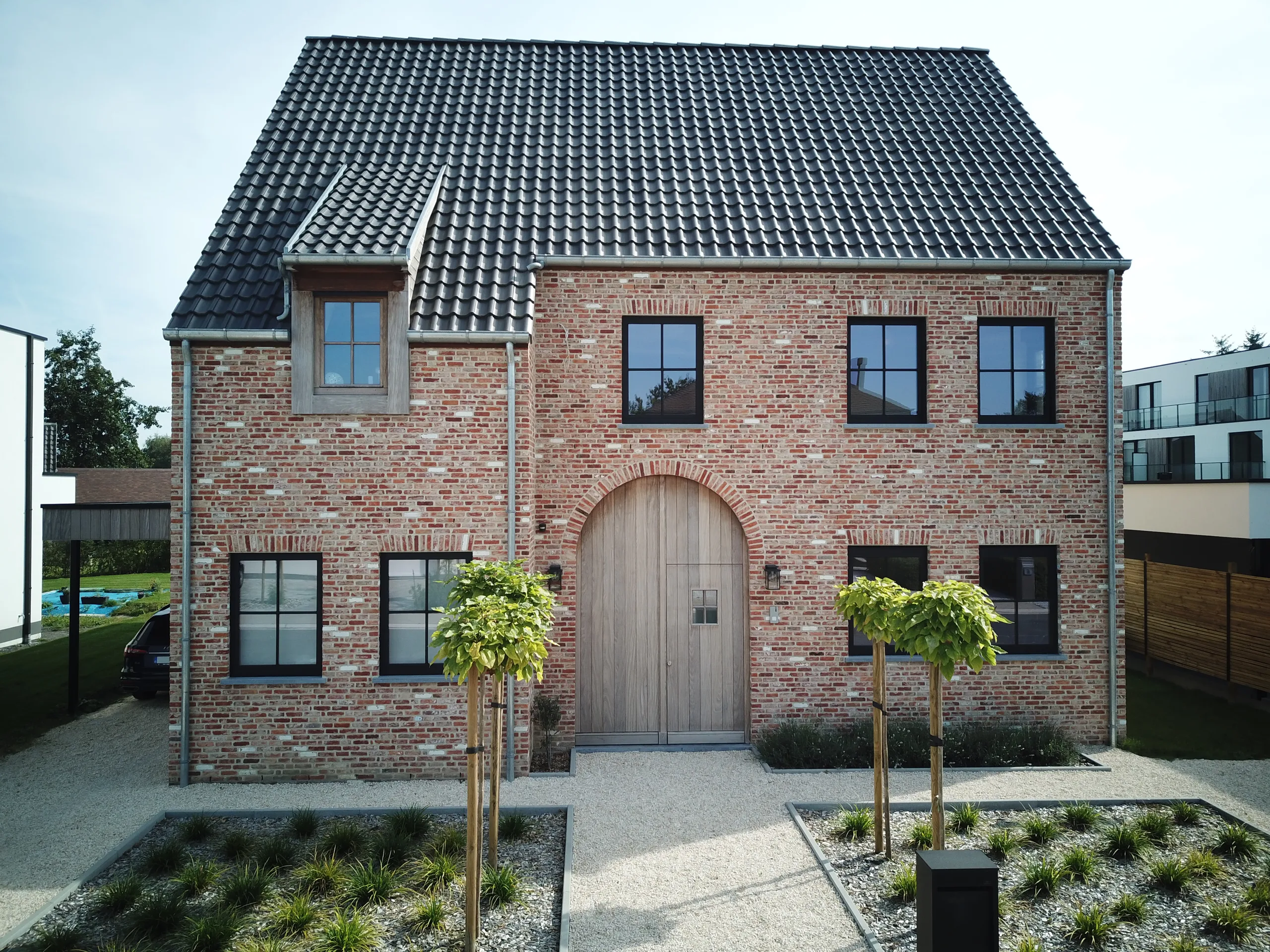 Voorgevel van een bakstenen woning met dakkapel, grote raampartijen en boogdeur