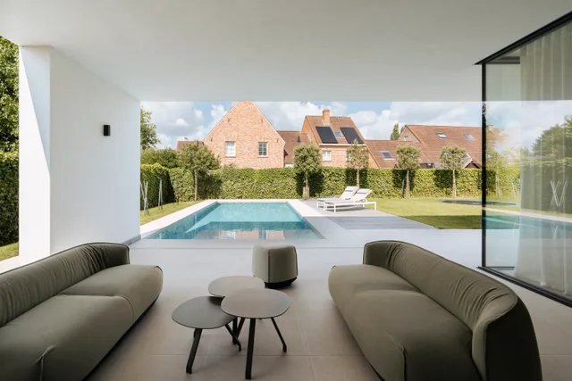 Moderne leefruimte met uitzicht op zwembad en tuin via grote glaspartijen