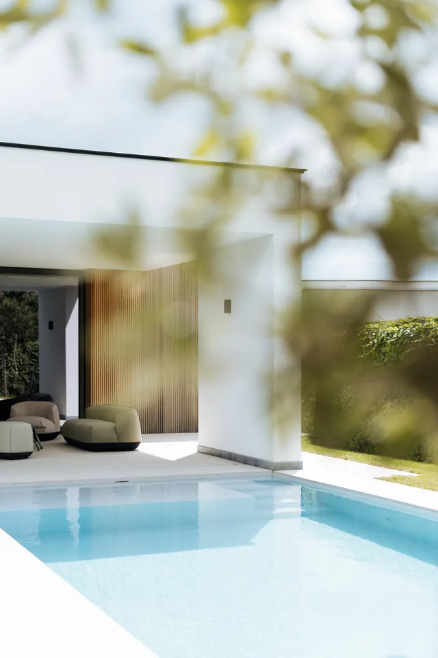 Moderne woning met zwembaad en loungeplek, uitkijkend op groene tuin achter glas