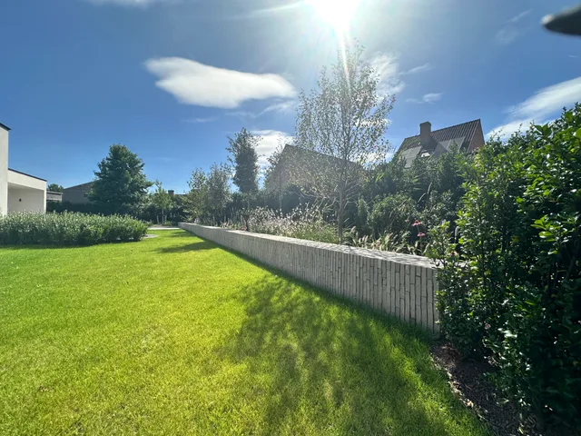Ruime tuin met gazon, houten afrastering en groene beplanting, uitgezicht op omliggende woningen