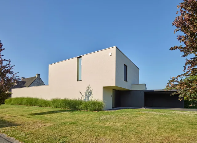 Moderne woning met witte gevel, grote raampartijen en integraal carport aan de zijkant