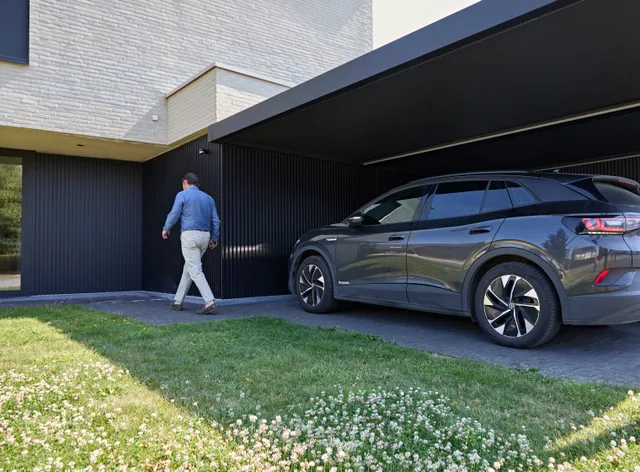 Man loopt naar moderne gesloten garage met zwarte lamellen naast geparkeerde auto