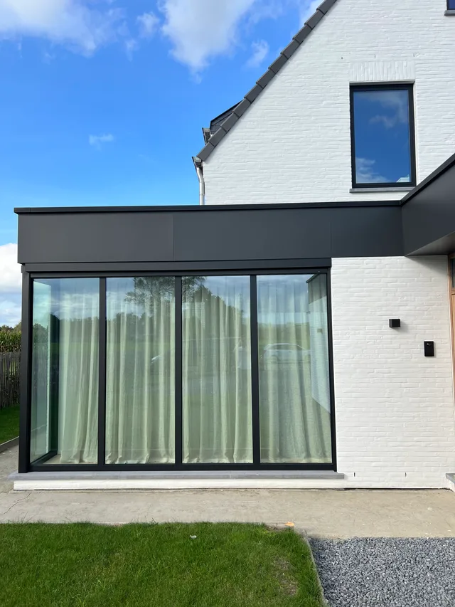 Moderne uitbouw met grote glazen schuifpuien en zwart stalen frame aan de tuinzijde van een woning