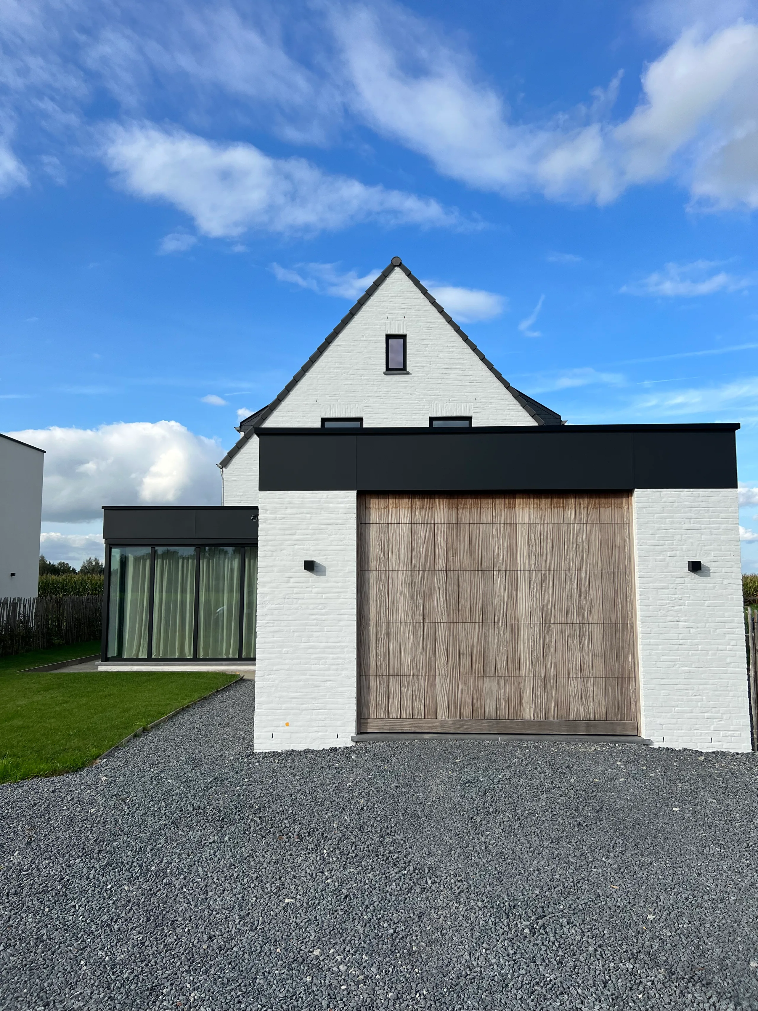 Moderne garage met witte gevelsteen, zwarte accenten en houten garagedeur, met tuinzijde
