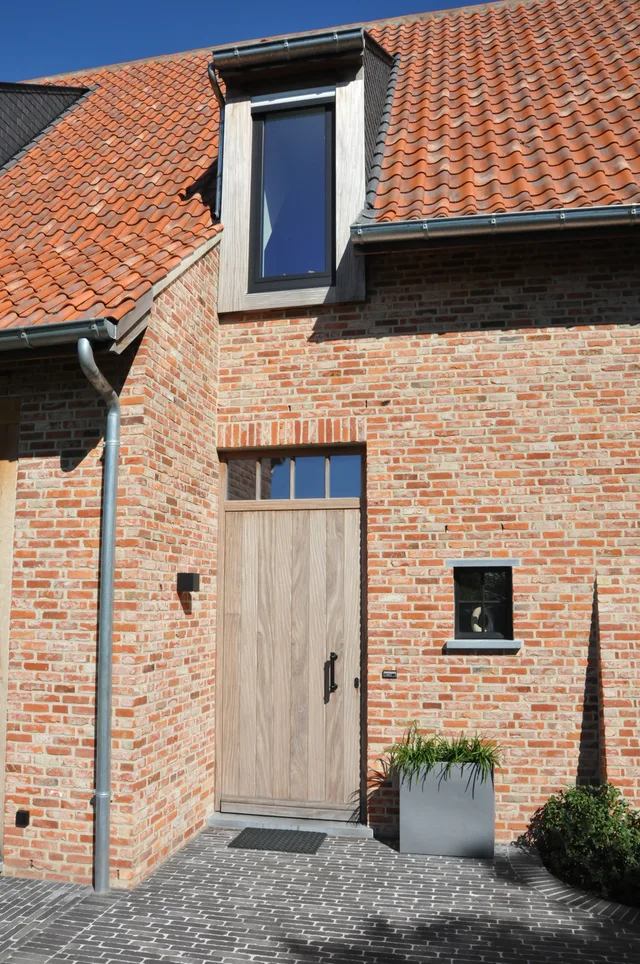 Voorgevel van een bakstenen woning met dakkapel, houten voordeur en terracotta dak