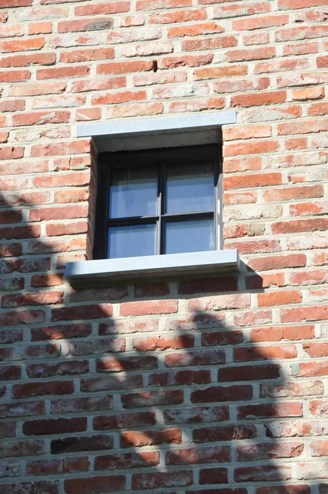 Detail van rode gevelsteen met modern zwart raamkozijn en witte bekroning