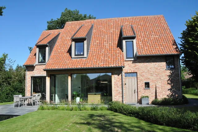 Woning met rode bakstenen gevel, groot glazen pui en drie dakkapellen op het dak