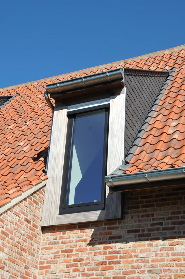 Dakkapel met witte houten kozijnen op pannendak met rode en grijze pannen