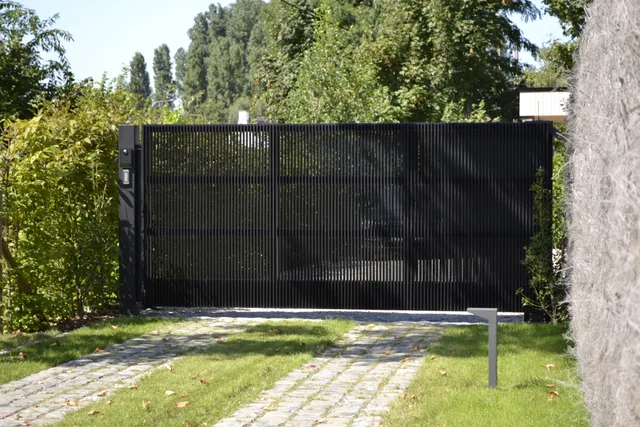 Moderne zwarte poort met verticale lamellen aan de ingang van een woning, aansluitend op een grijze muur