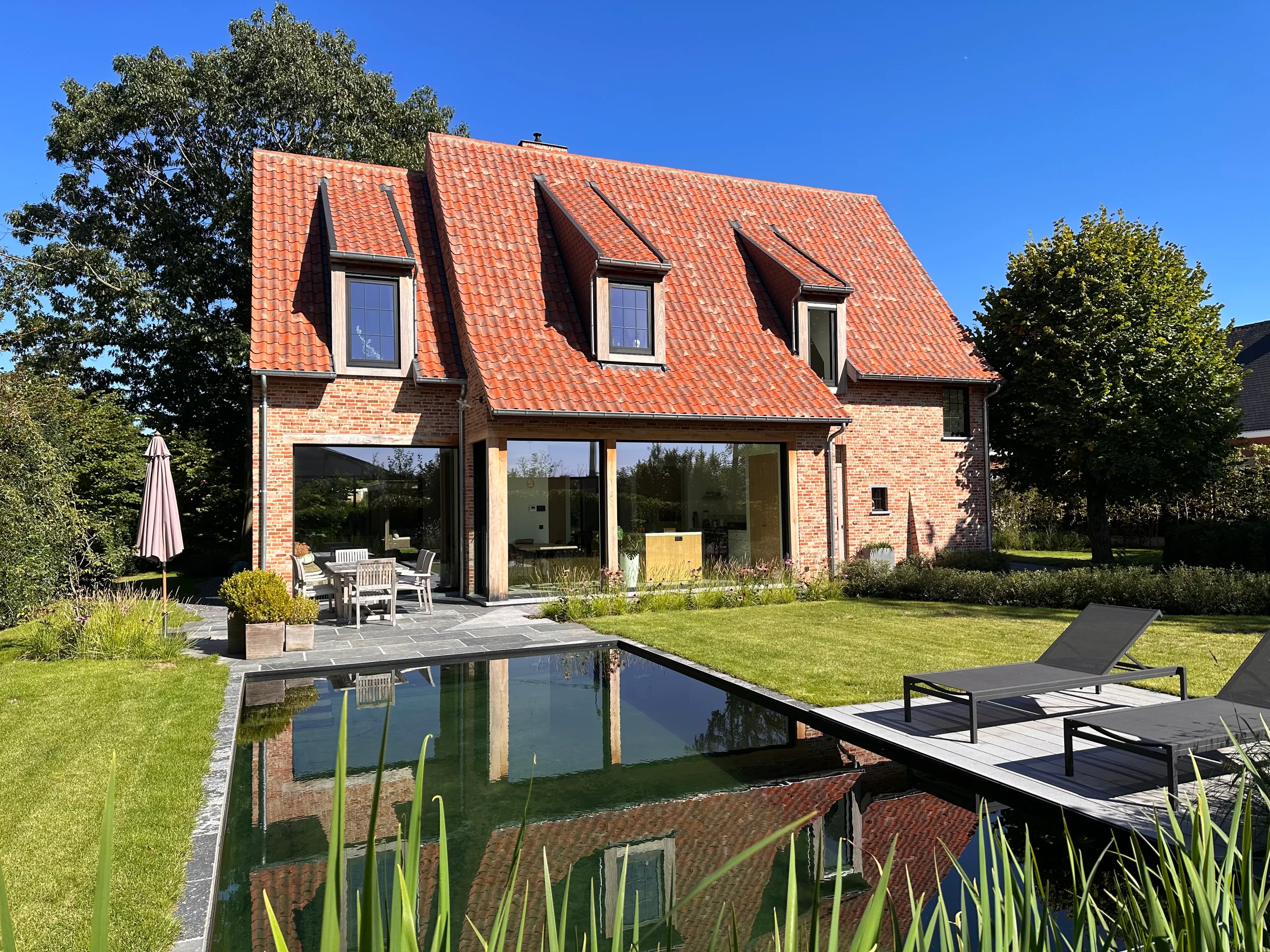 Achtergevel van bakstenen woning met dakkapels, grote raampartijen en zwembad in voortuin
