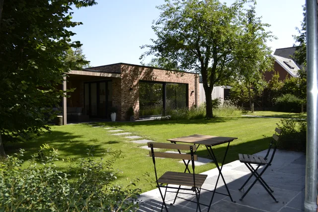 Moderne woning met baksteengevel en grote glaspartijen, gezien vanaf het terras met zicht op de tuin