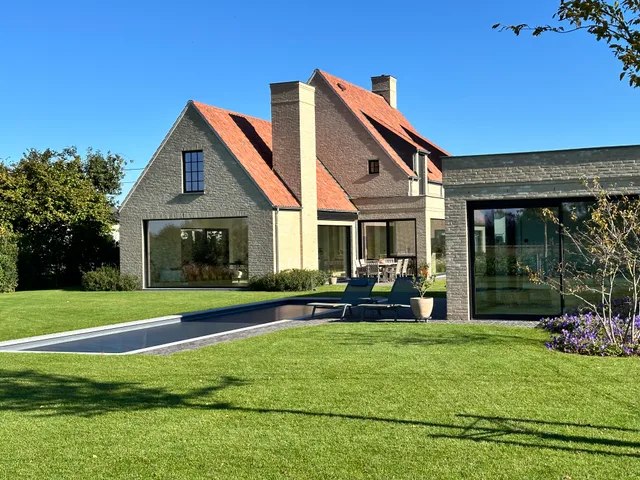 Moderne woning met bakstenen gevel, grote glaspartijen en aansluitend zwembad, gezien vanaf de tuin