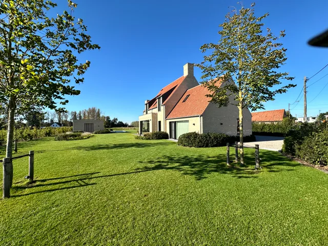 Moderne woning met pannendak en grijze gevelbekleding, omgeven door groen gazon en jonge bomen