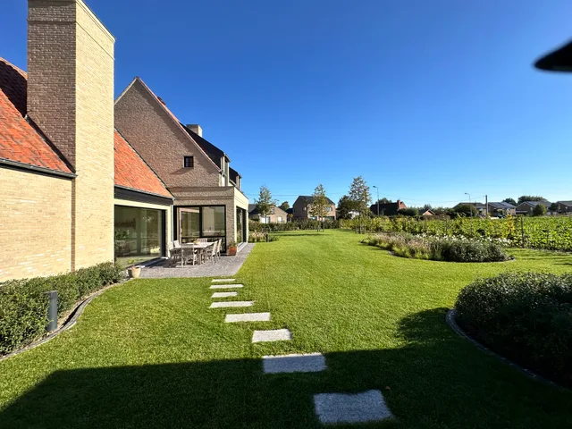 Woning met tuinzijde, grote glazen ramen en voorbouw die uitgeeft op groene tuin met stenen stappen