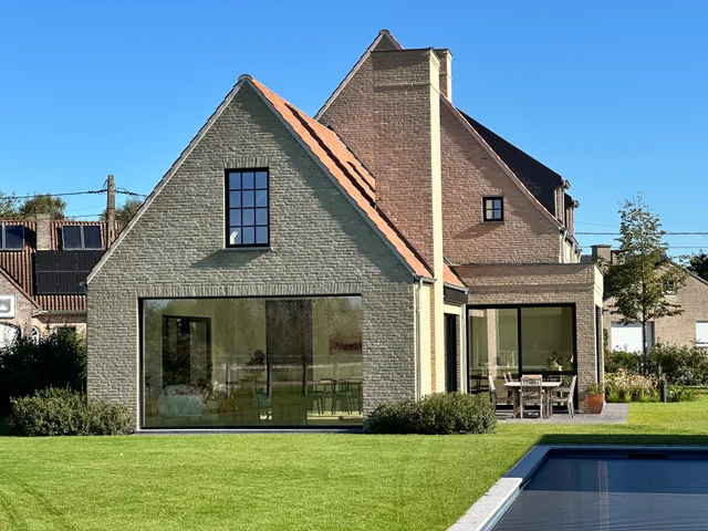Moderne woning met traditionele bakstenen gevel en grote glazen schuifpuien aan tuinzijde