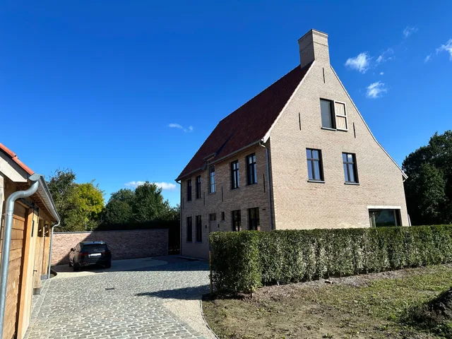 Nieuwbouwwoning met witte baksteengevel, donker dak en moderne raamindeling aan oprit
