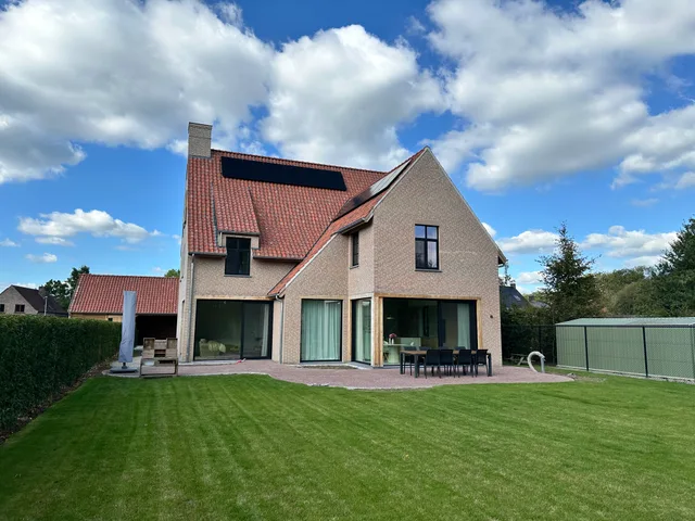 Tuinzijde van een moderne woning met bakstenen gevel, rode dakpannen en grote glazen schuifdeuren die uitkomen op een gr
