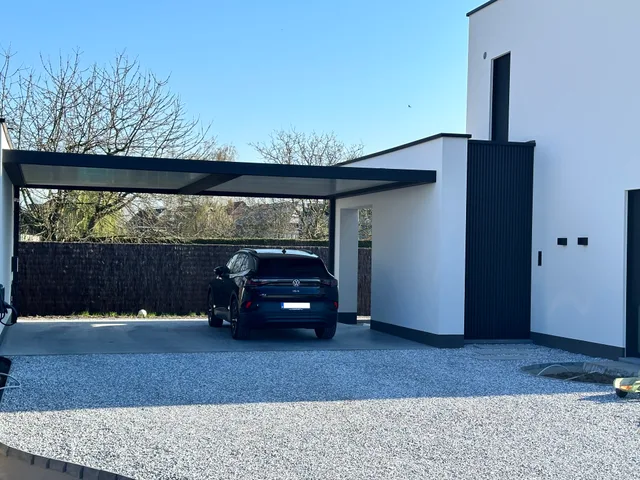 Moderne woning met witte crepi en zwarte accenten, carport met glazen wand en oprit in grind