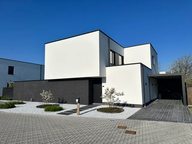 Moderne woning met witte gevel en zwarte baksteensokkel, voortuin met grind en inrit