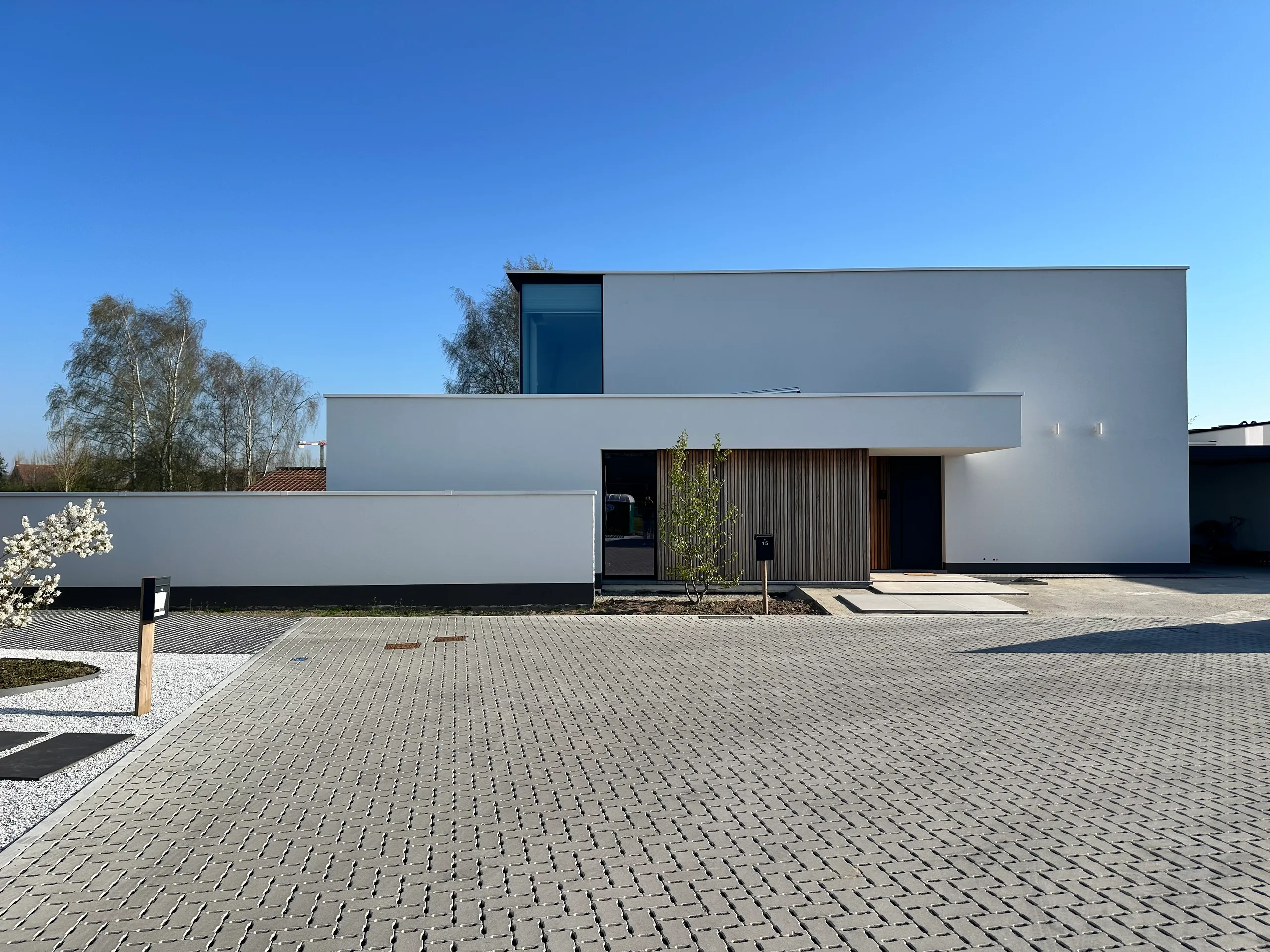 Moderne woning met witte crepi-gevel, grote raampartijen en verharde voortuin