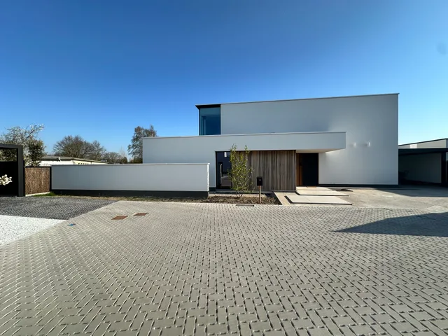 Moderne woning met witte crepi, trappenstructuur en ingang onder overkapping aan een geplaveide oprit