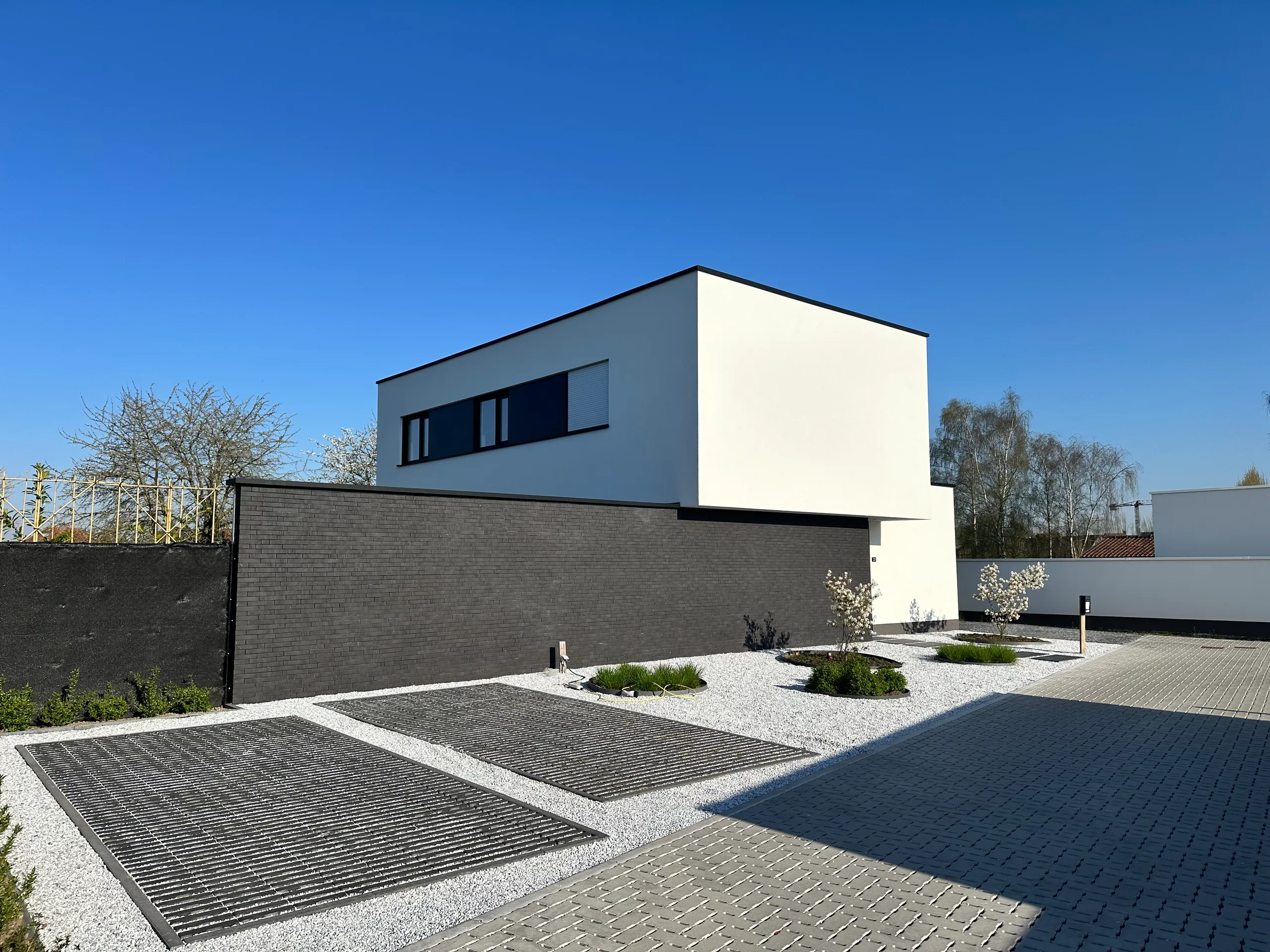 Moderne woning met witte bovenbouw en grijze gevelsteen, voortuin met grind en grijze betonnen parkeervakken