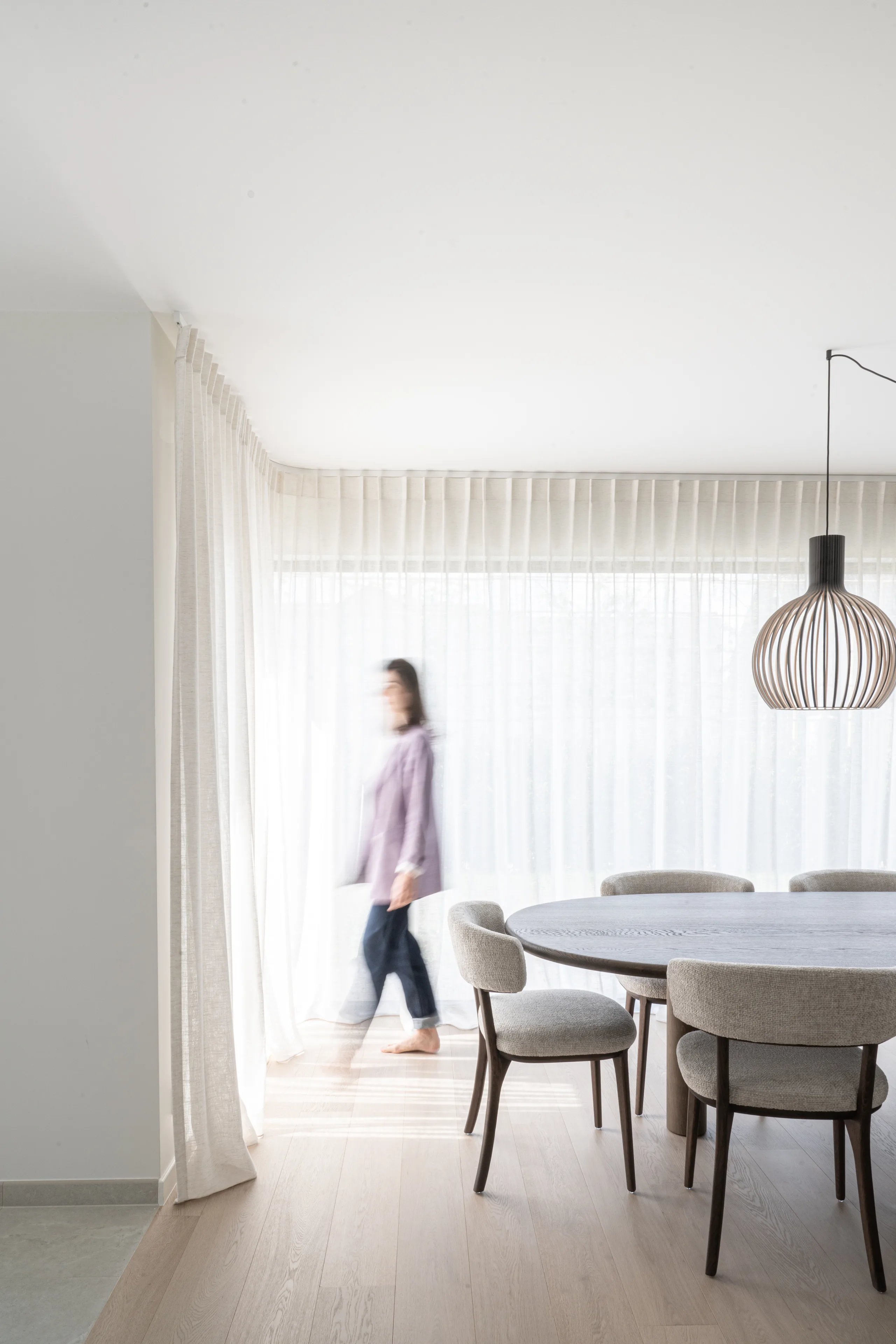 Eethoek met ronde tafel en stoelen onder hangende lamp, toegang tot tuinzijde met lange gordijnen