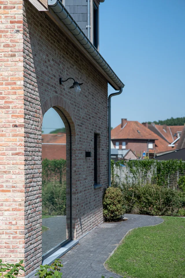 Tuinzijde van een moderne woning met grote gebogen raampartij en rode bakstenen gevel