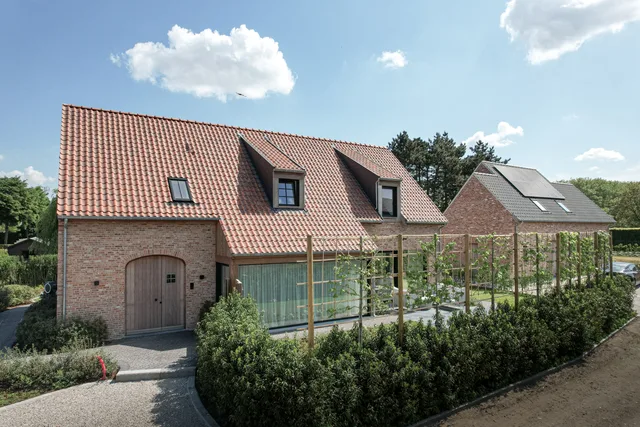 Nieuwbouwwoning met rode dakpannen, bakstenen gevel en moderne uitbouw met glazen wand en houten overkapping
