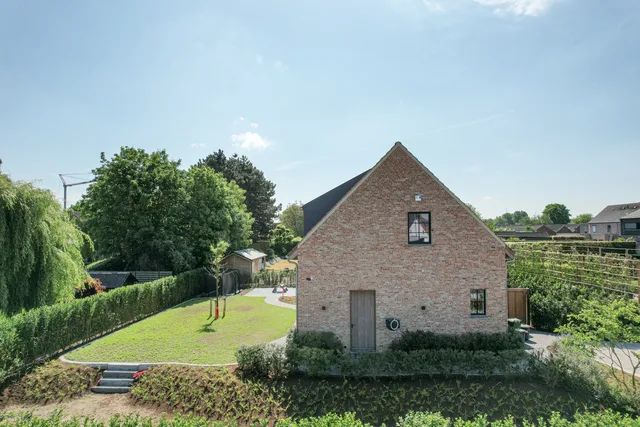 Nieuwbouwwoning met bakstenen gevel en puntdak in landelijke omgeving met tuin