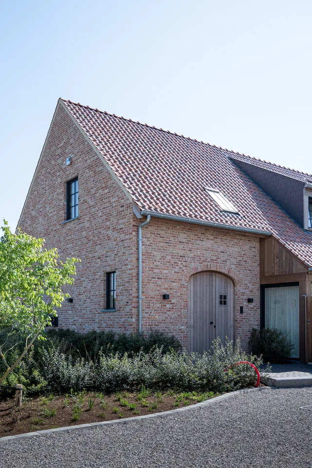 Voorgevel van een bakstenen woning met zadeldak en rode dakpannen