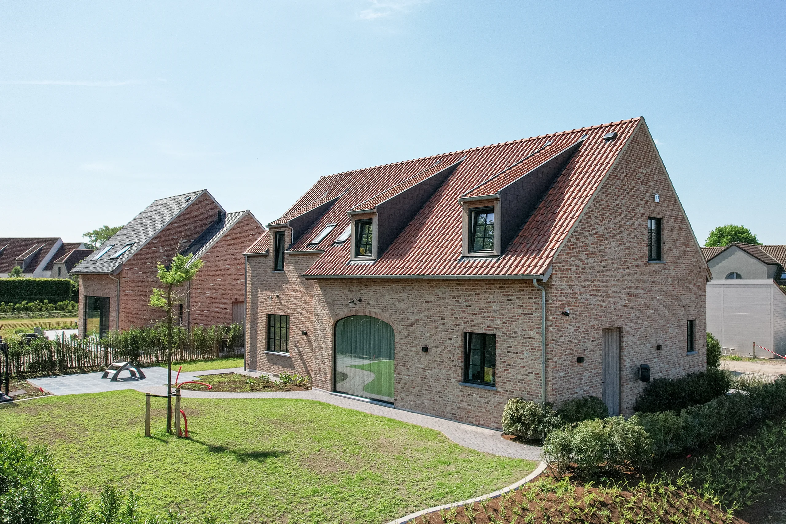Voorgevel van een moderne bakstenen woning met rode dakpannen en dakkapels