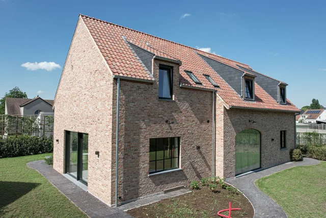 Nieuwbouwwoning met bakstenen gevel, oranje dakpannen en dakkapellen, omgeven door tuin