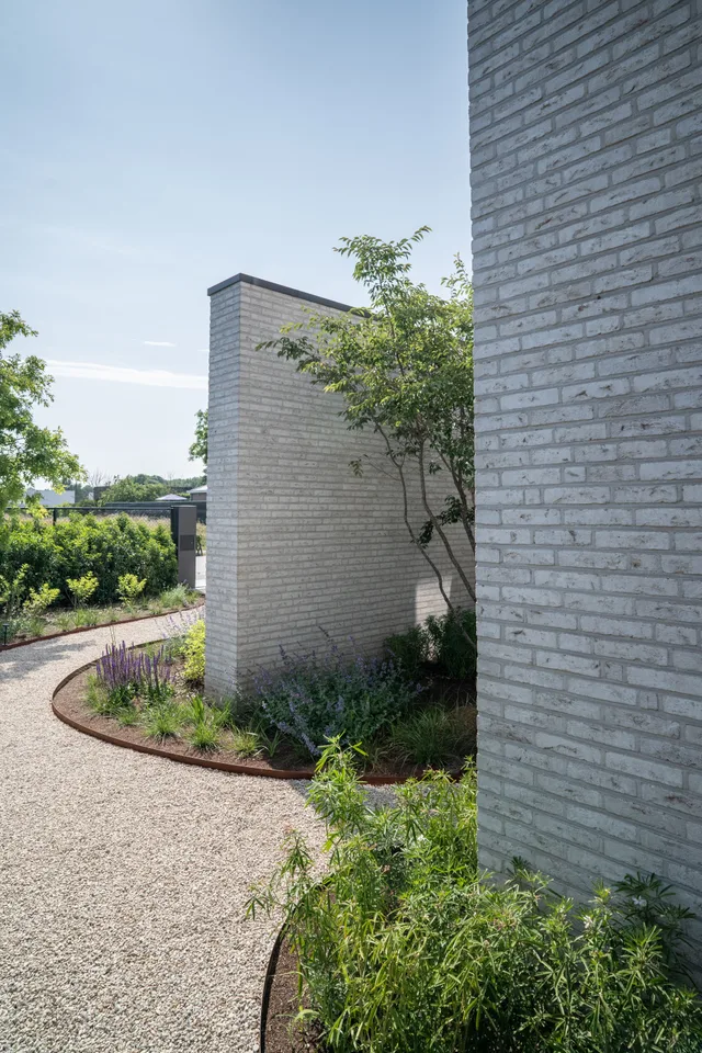Ruime tuin met grindpad langs moderne bakstenen woning met aangeplante struiken en jonge bomen