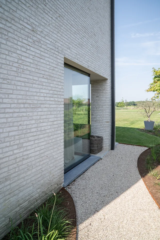 Moderne bakstenen woning met groot raampartij aan entree die uitzicht geeft op groene tuin