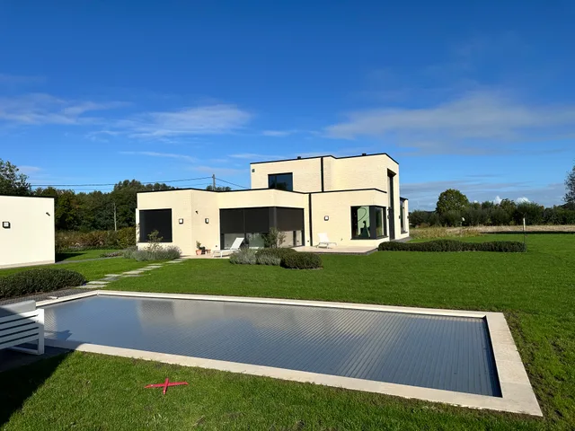 Moderne woning met witte gevel en grote raampartijen, gezien vanaf de voortuin met zwembad