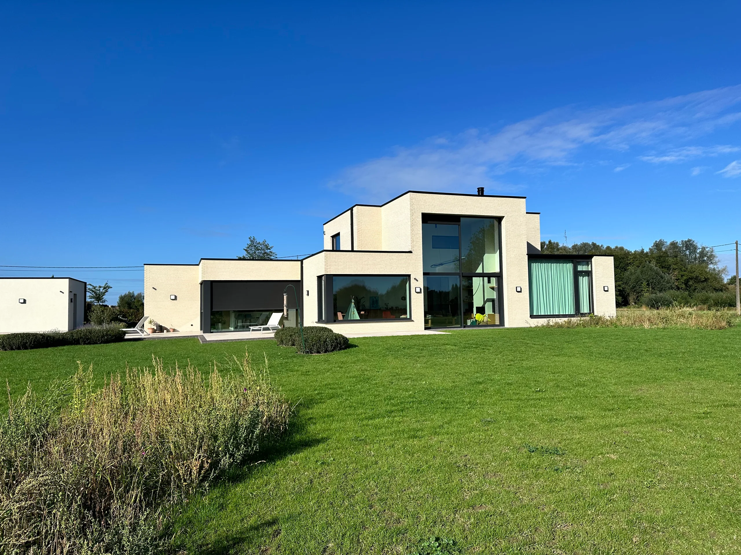 Moderne woning met crèmekleurige gevelbekleding en grote glaspartijen, omgeven door groen gazon