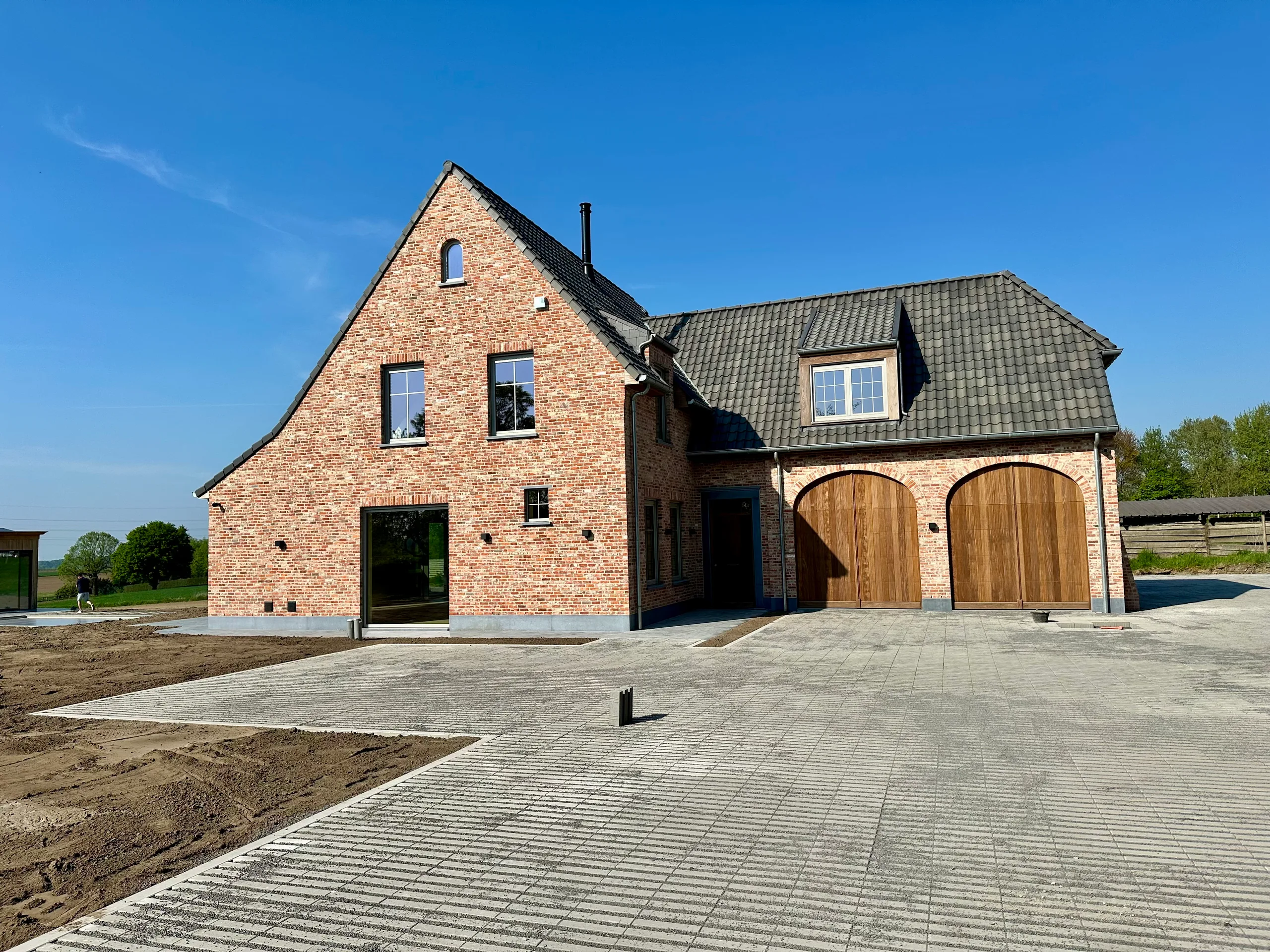 Voorgevel van een nieuwbouwwoning in baksteen met houten garagepoortes en aangelegde oprit