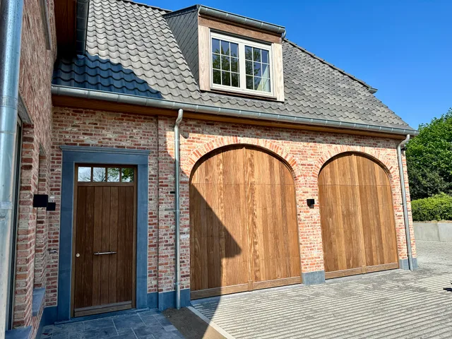 Voorgevel van een bakstenen woning met houten garagetdeuren en dakkapel