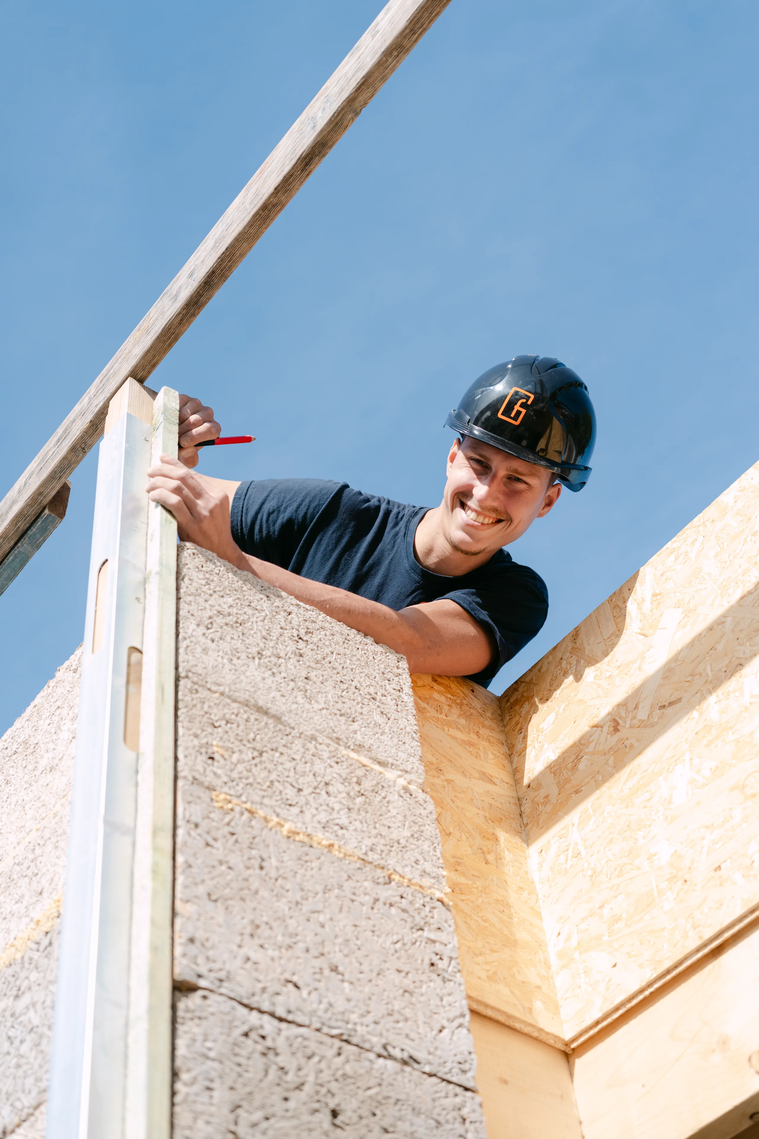 Werker met helm meet en markeert een betonnen gevelwand op een bouwwerf onder blauwe hemel